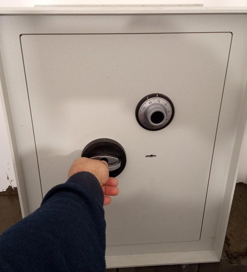 A person's hand gripping the handle of a large beige electronic and dial combination safe door.
